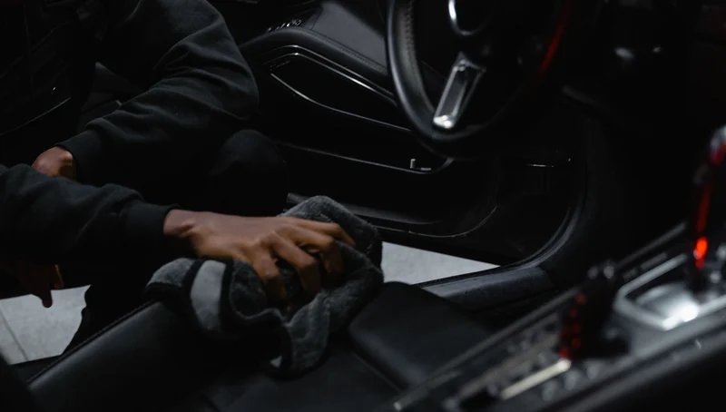 Cleaning a dark leather seat with a microfibre cloth.
