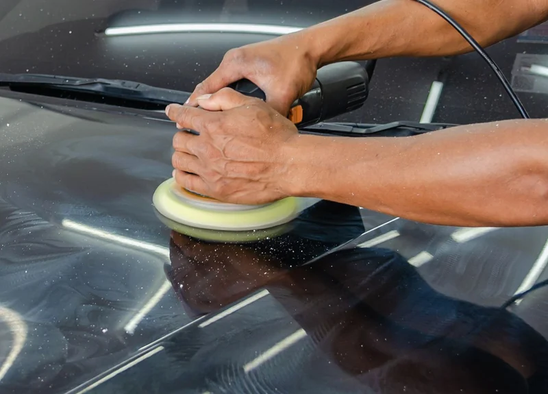 Hands guiding a polisher over a car’s paintwork.